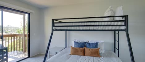 Una cama litera con ropa de cama a rayas y dos almohadas, una terraza de madera y una puerta corrediza al balcón.