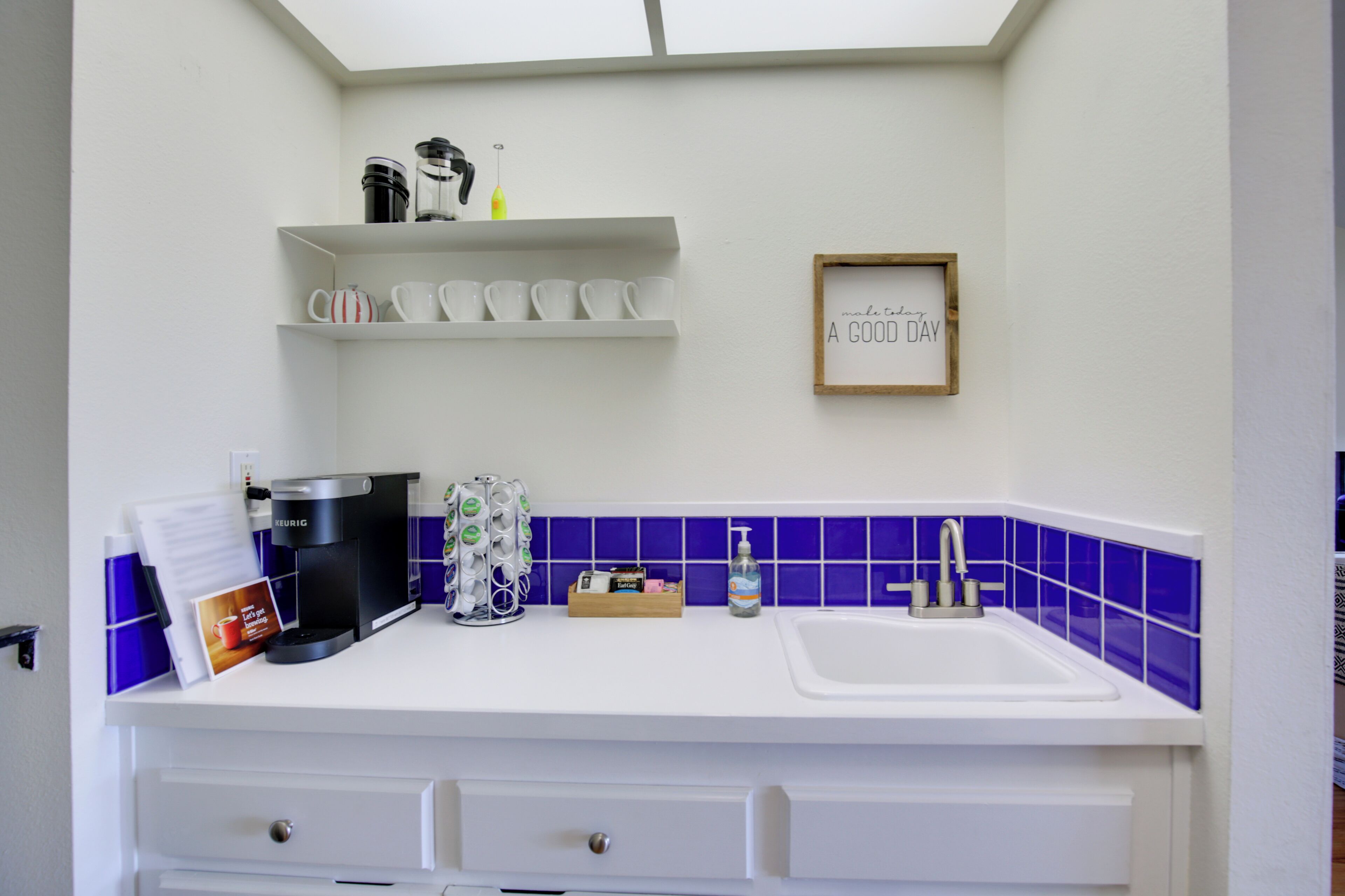 A modern kitchen with white cabinetry, a coffee maker, a sink, and a blue-tiled backsplash.