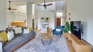 Un salón amplio con sofá, sillones, una mesa de centro y televisor. Se observa una cocina al fondo, con armarios y una zona de comedor.