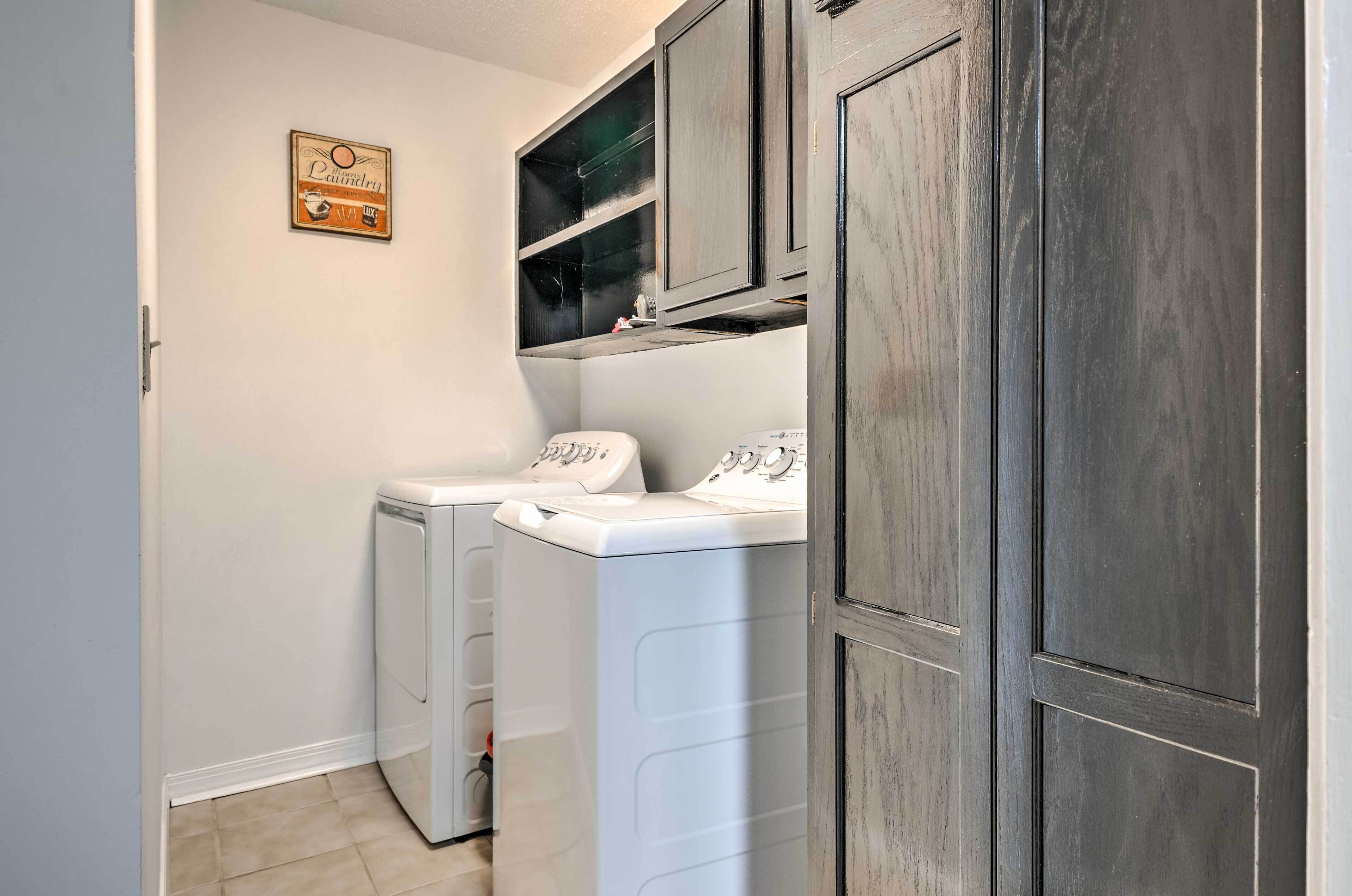 A laundry room with two front-loading washing machines, a dryer, and a wall-mounted cabinet above the machines.