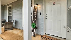 A porch with a wicker chair, a welcome sign, and a white door. - Ocean Springs Home w/ Sunroom ~ 5 Mi to Beach (Ocean Springs)