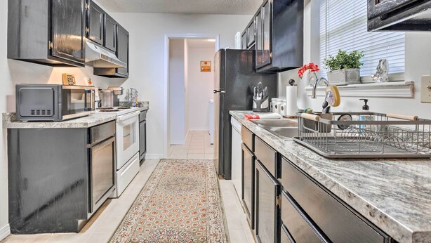 Une cuisine moderne avec des meubles de couleur sombre, des appareils électroménagers en acier inoxydable et un tapis à motifs.