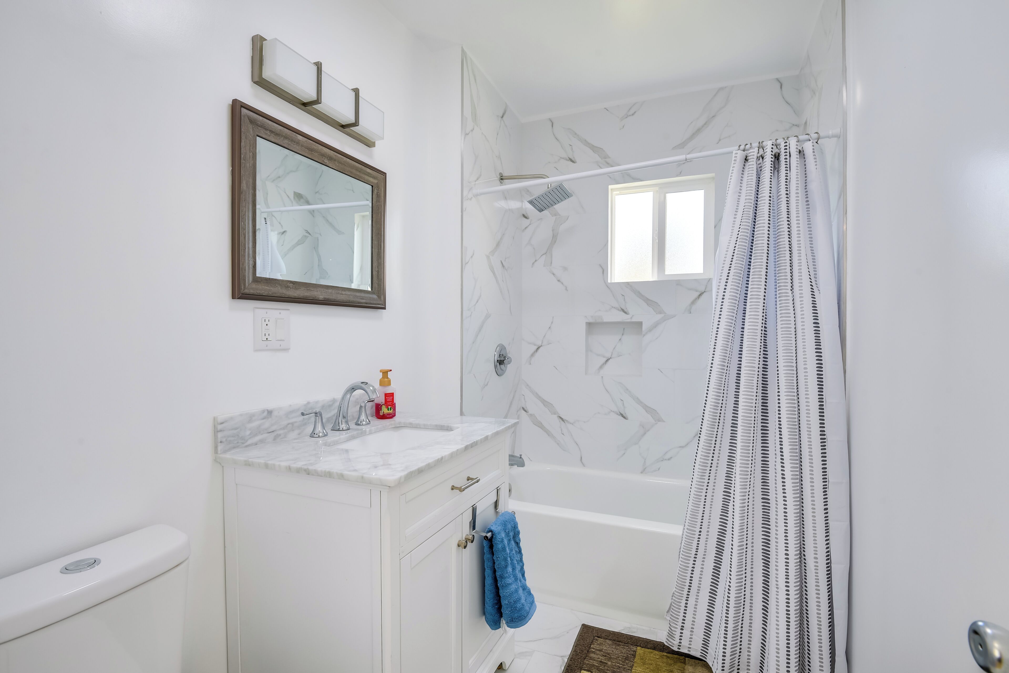 A bathroom with a marble sink, a toilet, a bathtub, and a shower curtain.