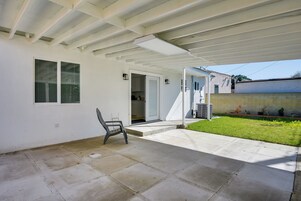 Un patio techado con piso de concreto, una puerta que da a un espacio interior y un pequeño césped con una silla.