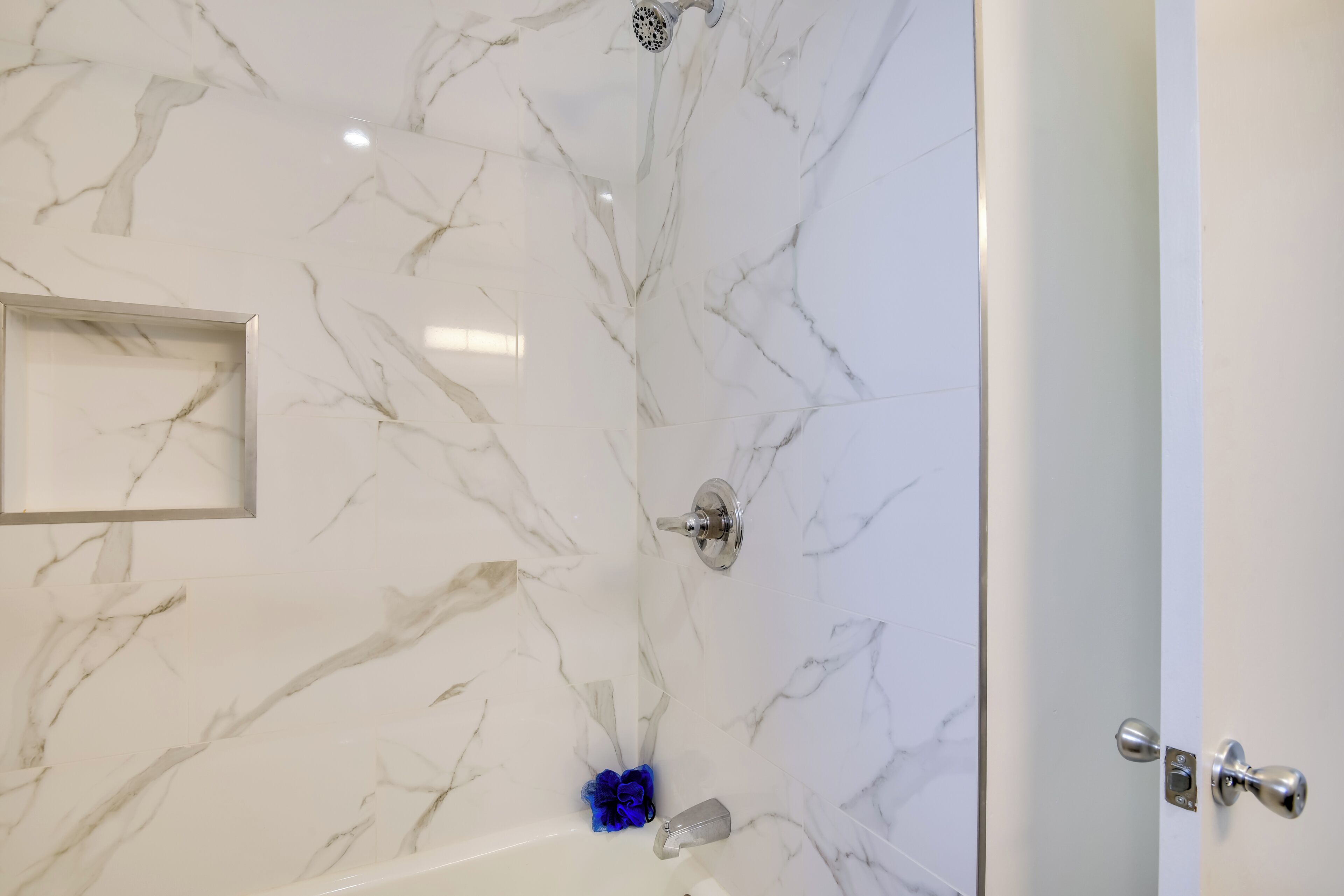 Ein Badezimmer mit Marmorwänden, einer Dusche und einer Tür mit silbernem Griff.