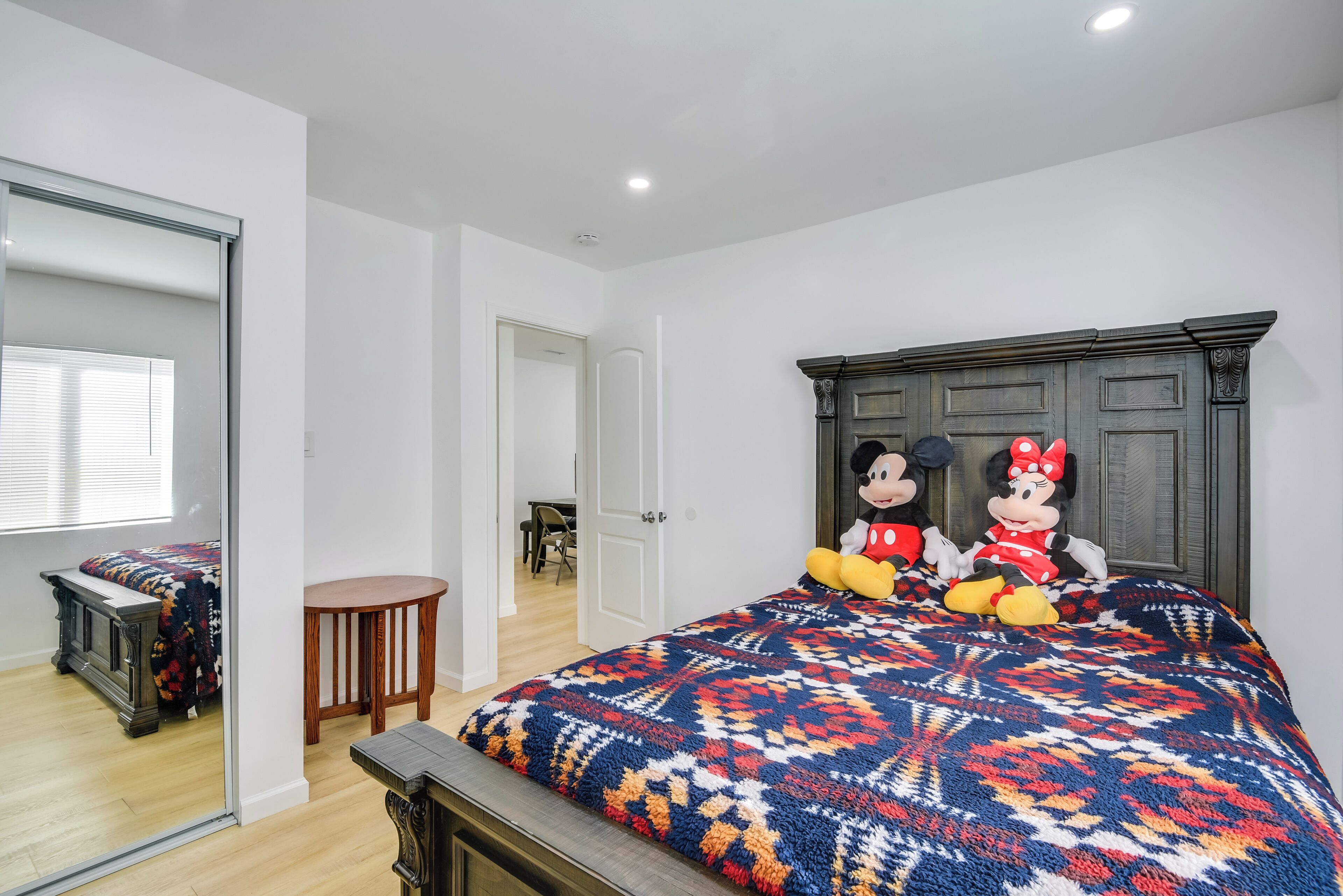 Een slaapkamer met een groot bed, twee zachte Mickey Mouse en Minnie Mouse knuffels, een houten hoofdbord en een spiegel.
