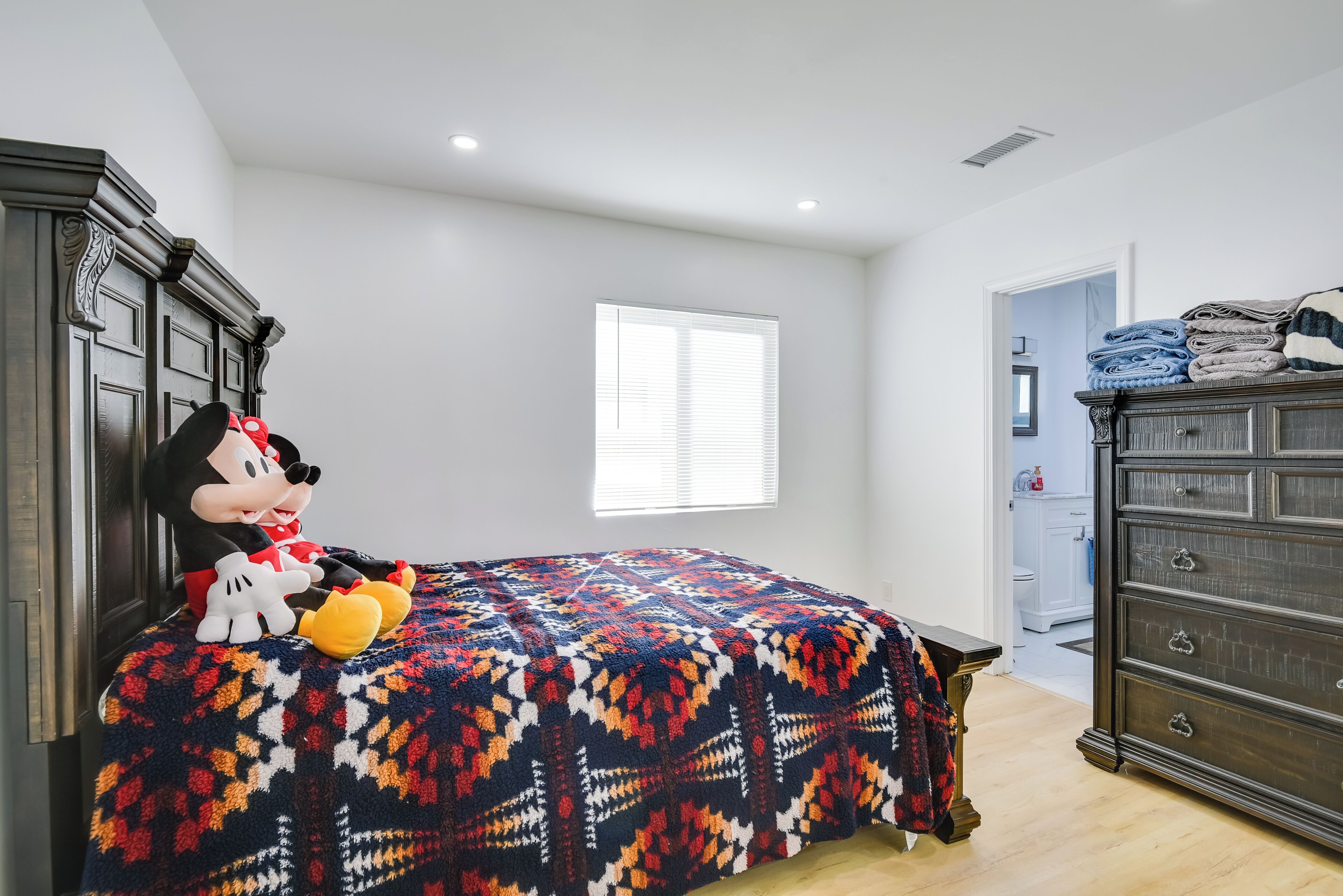 Quarto com uma cama, penteadeira e um boneco de pelúcia do Mickey Mouse.