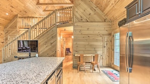 A wooden cabin interior with a kitchen, dining area, and a staircase.