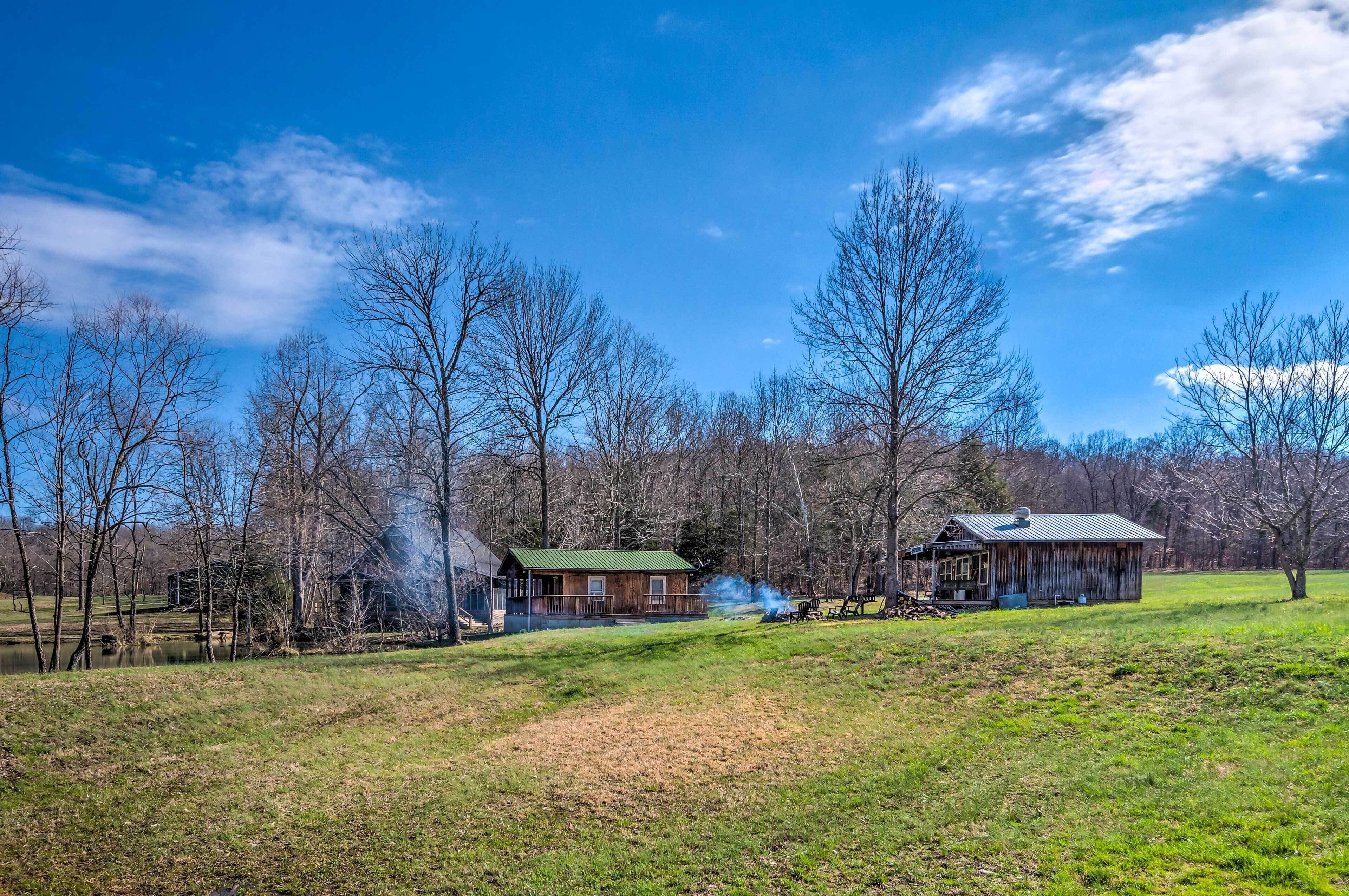 A rural landscape with two wooden cabins, a clear blue sky, and a pond.