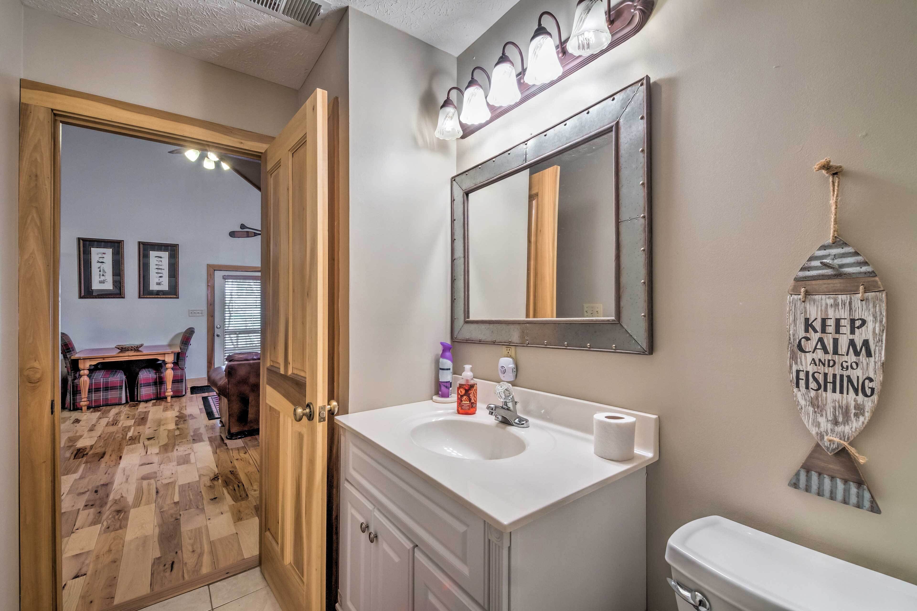 A bathroom with a white sink, mirror, and toilet. There is a wooden door leading to a dining area with a table and chairs.