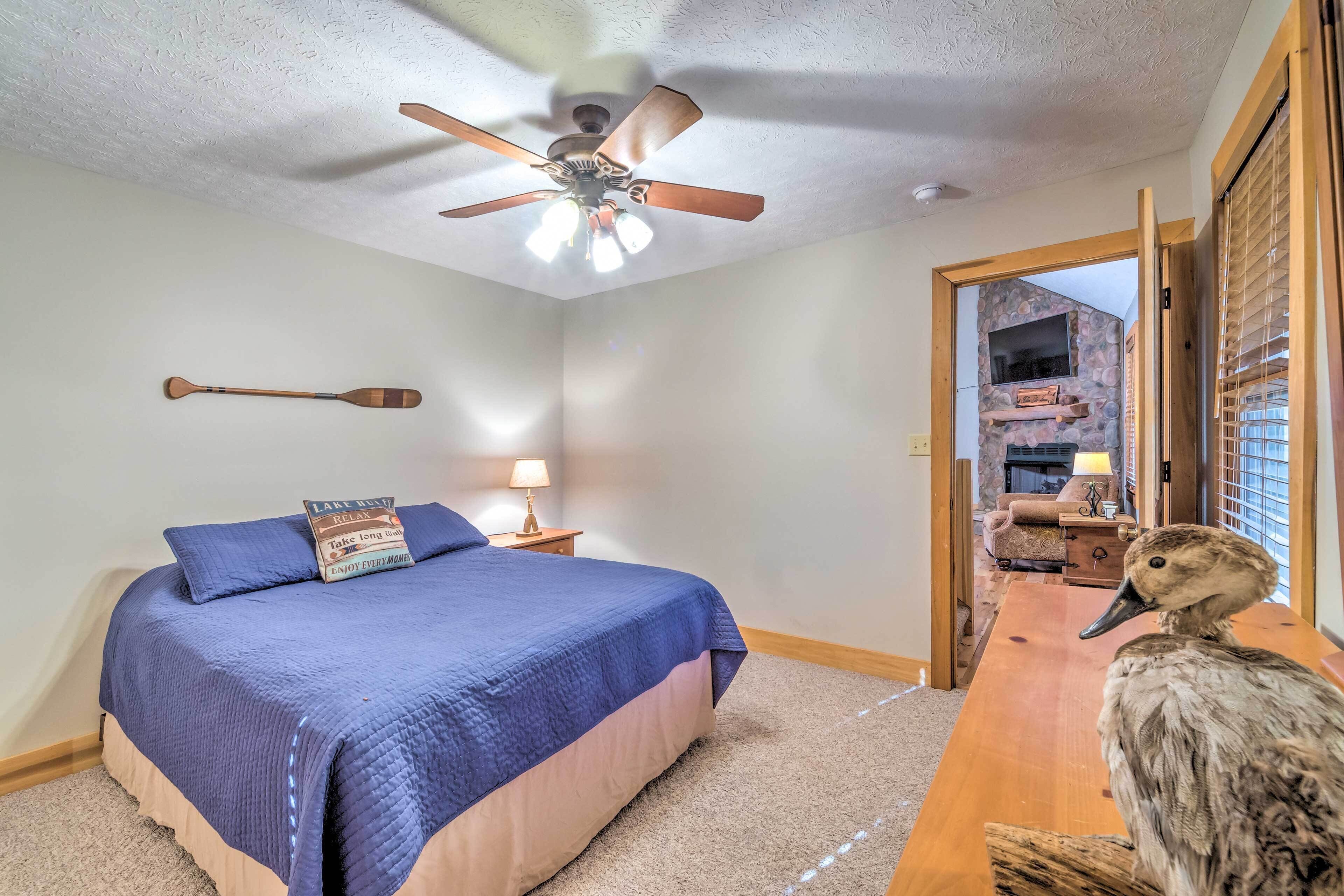 Une chambre à coucher avec un lit, un ventilateur de plafond, une planche de paddle en bois et une table en bois sur laquelle est posé un canard.