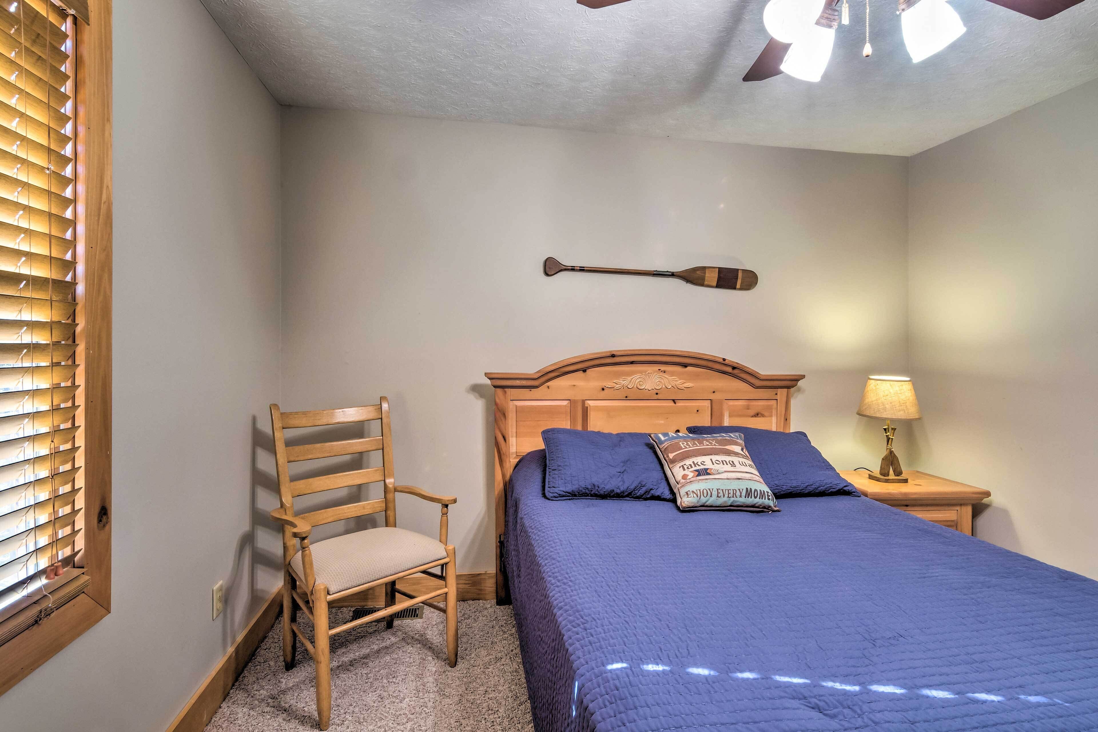 A bedroom with a bed, a wooden chair, a nightstand with a lamp, and a ceiling fan.