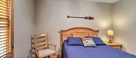 A bedroom with a bed, a wooden chair, a nightstand with a lamp, and a ceiling fan.