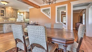 Un'area pranzo con tavolo in legno e sedie a motivi, un lampadario e una cucina sullo sfondo.