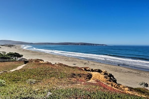 Paisagem costeira com uma praia arenosa, afloramentos rochosos e um céu azul límpido.