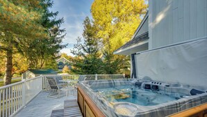Ein Whirlpool auf einer Holzterrasse mit Blick auf ein Haus und Bäume.