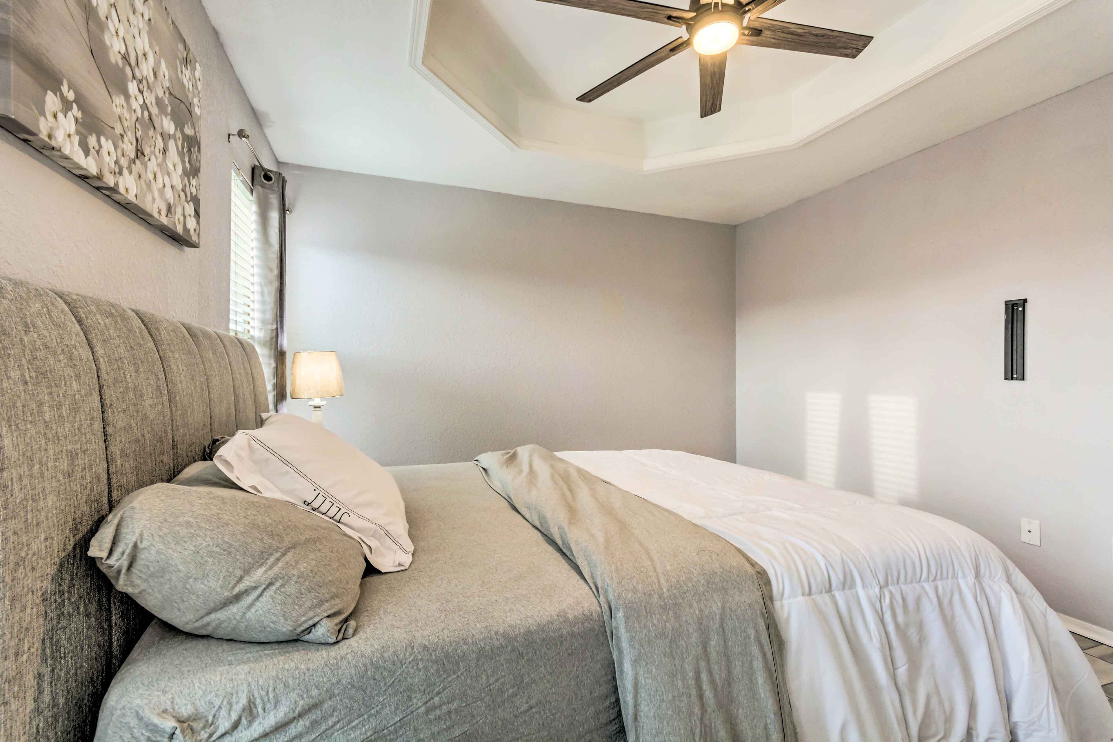 Un dormitorio con cama, ventilador de techo, mesita de noche y lámpara de pared.