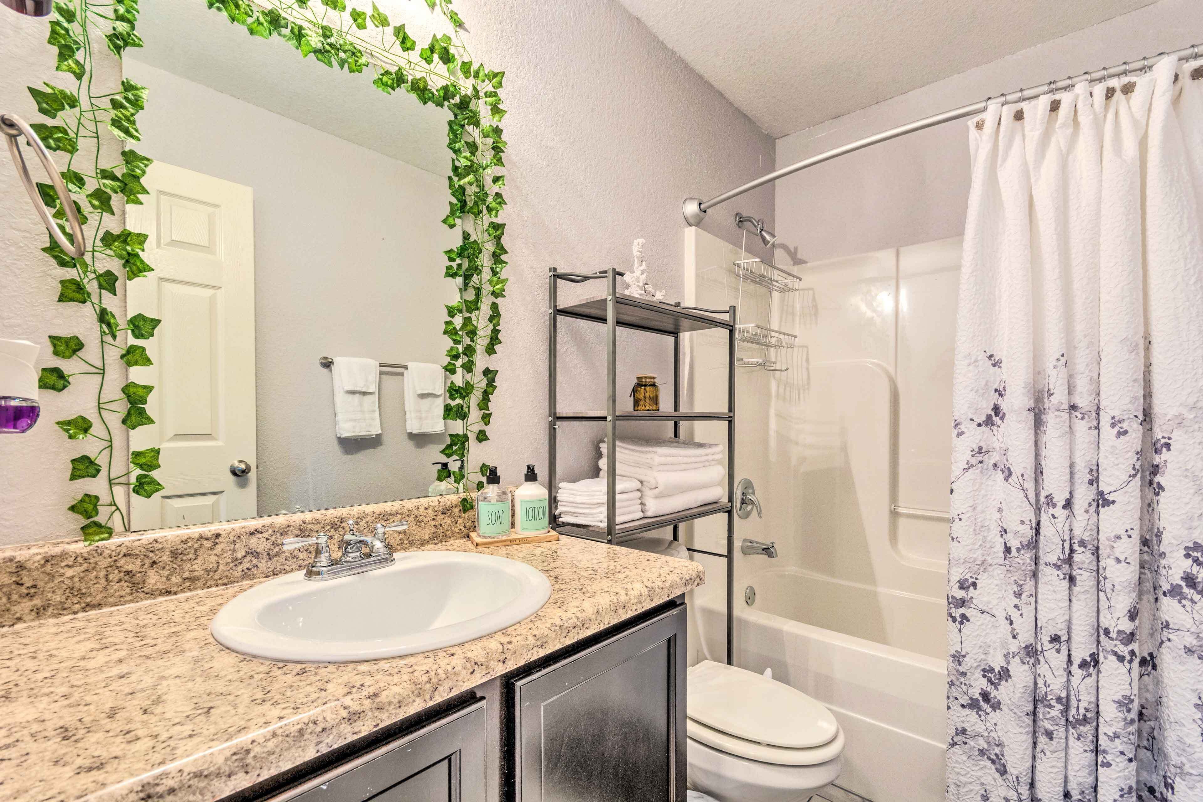 A bathroom with a granite countertop sink, a mirror, a glass shower enclosure, and a shower curtain with a floral pattern.