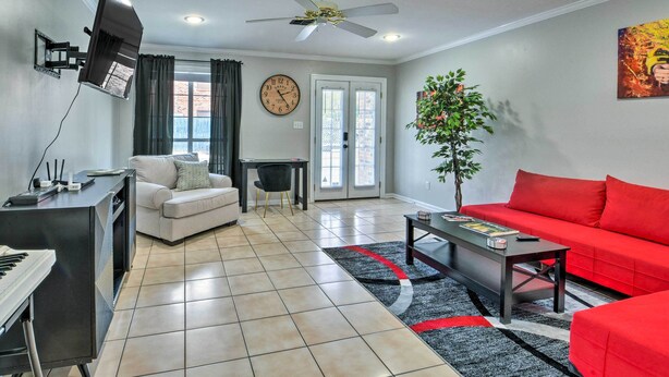 A living room with a sofa, a red couch, a coffee table, a TV mounted on the wall, a clock, and a ceiling fan. - Pet-friendly Lafayette Vacation Rental! (Lafayette)