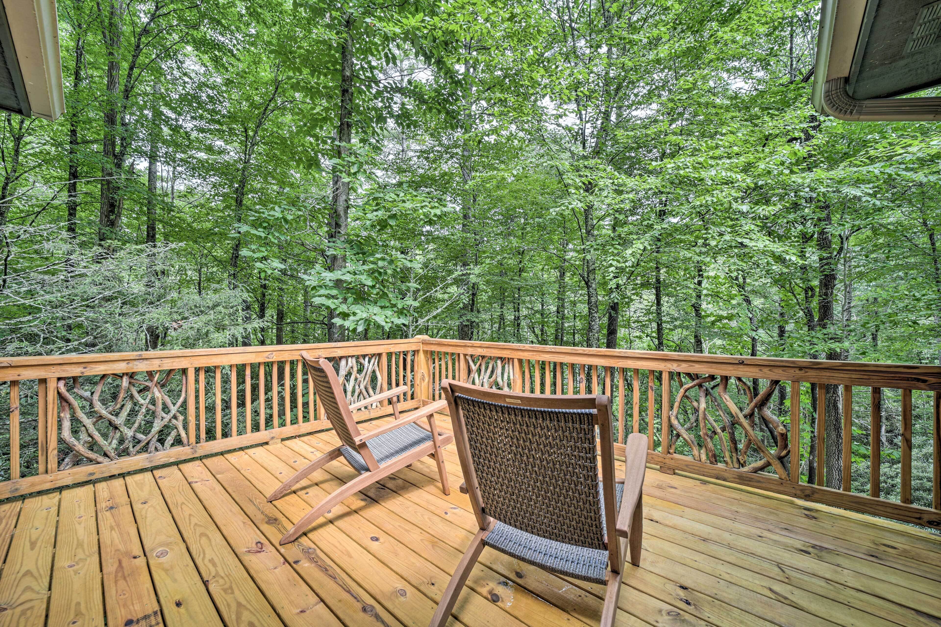 Eine Holzterrasse mit zwei Schaukelstühlen mit Blick auf einen Wald.