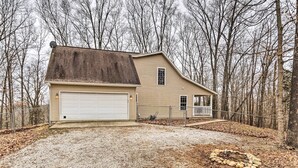 A single-story house with a garage, surrounded by a gravel driveway and a fire pit in the yard. - Serene Bloomington Home: Deck & Forest Views (Bloomington)
