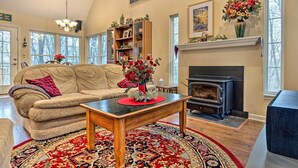 A cozy living room with a sofa, a coffee table, a fireplace, and a bookshelf. - Serene Bloomington Home: Deck & Forest Views (Bloomington)