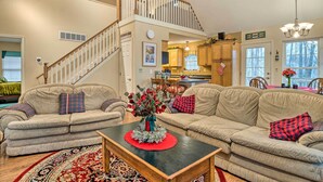 A spacious living room with a high ceiling, a wooden staircase, and a kitchen in the background. - Serene Bloomington Home: Deck & Forest Views (Bloomington)