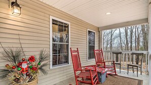 A porch with two rocking chairs, a potted plant with festive decorations, and a view of trees through the windows. - Serene Bloomington Home: Deck & Forest Views (Bloomington)