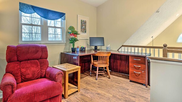 A compact office space with a red chair, a desk with drawers, a computer, and a window with a blue curtain. - Serene Bloomington Home: Deck & Forest Views (Bloomington)