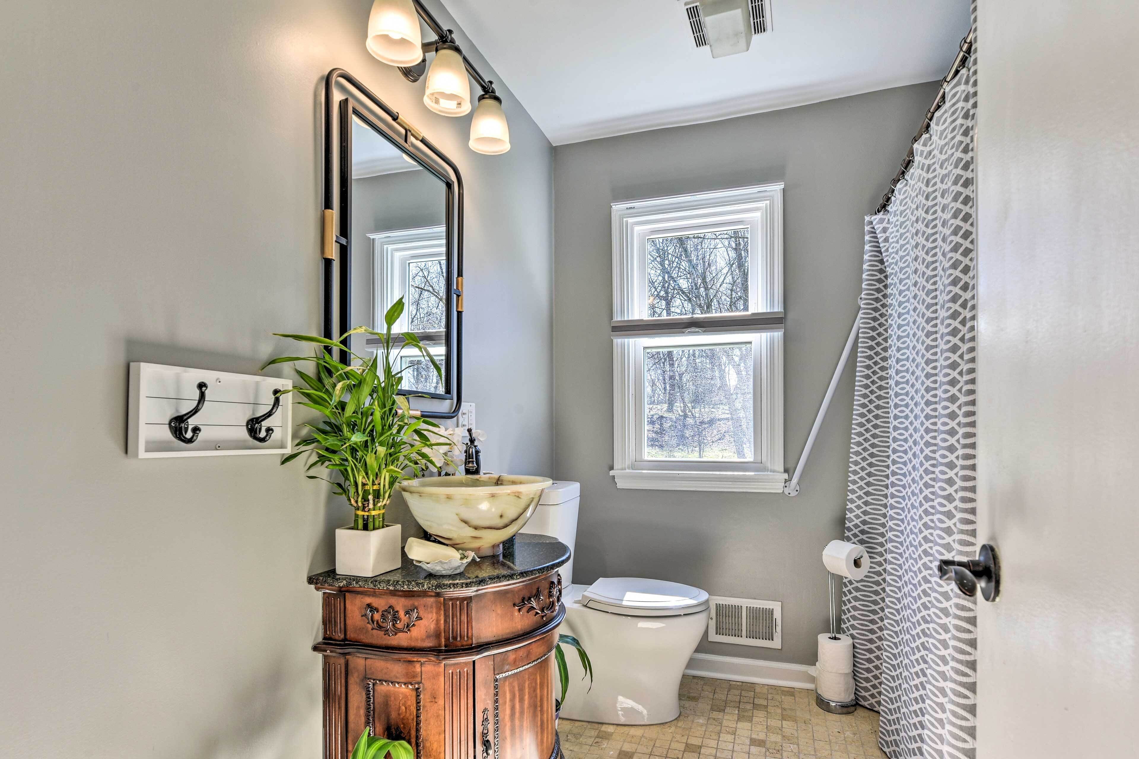 Une salle de bain comprenant un meuble-lavabo, un grand miroir, un lavabo avec une cuve, des toilettes et un rideau de douche.