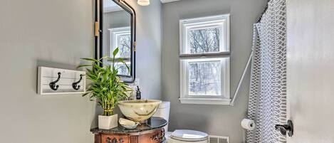 Une salle de bain comprenant un meuble-lavabo, un grand miroir, un lavabo avec une cuve, des toilettes et un rideau de douche.