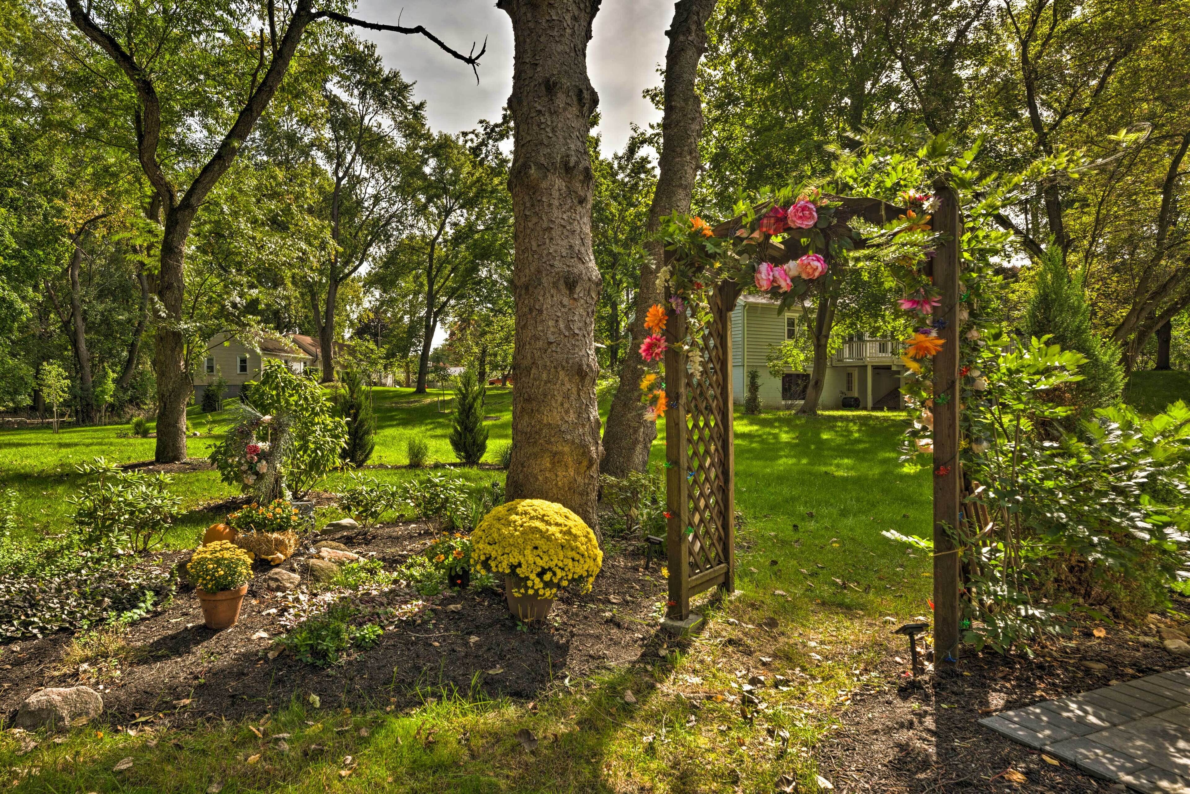 A garden with a wooden arbor covered in flowers, a house in the background, and a well-maintained lawn.