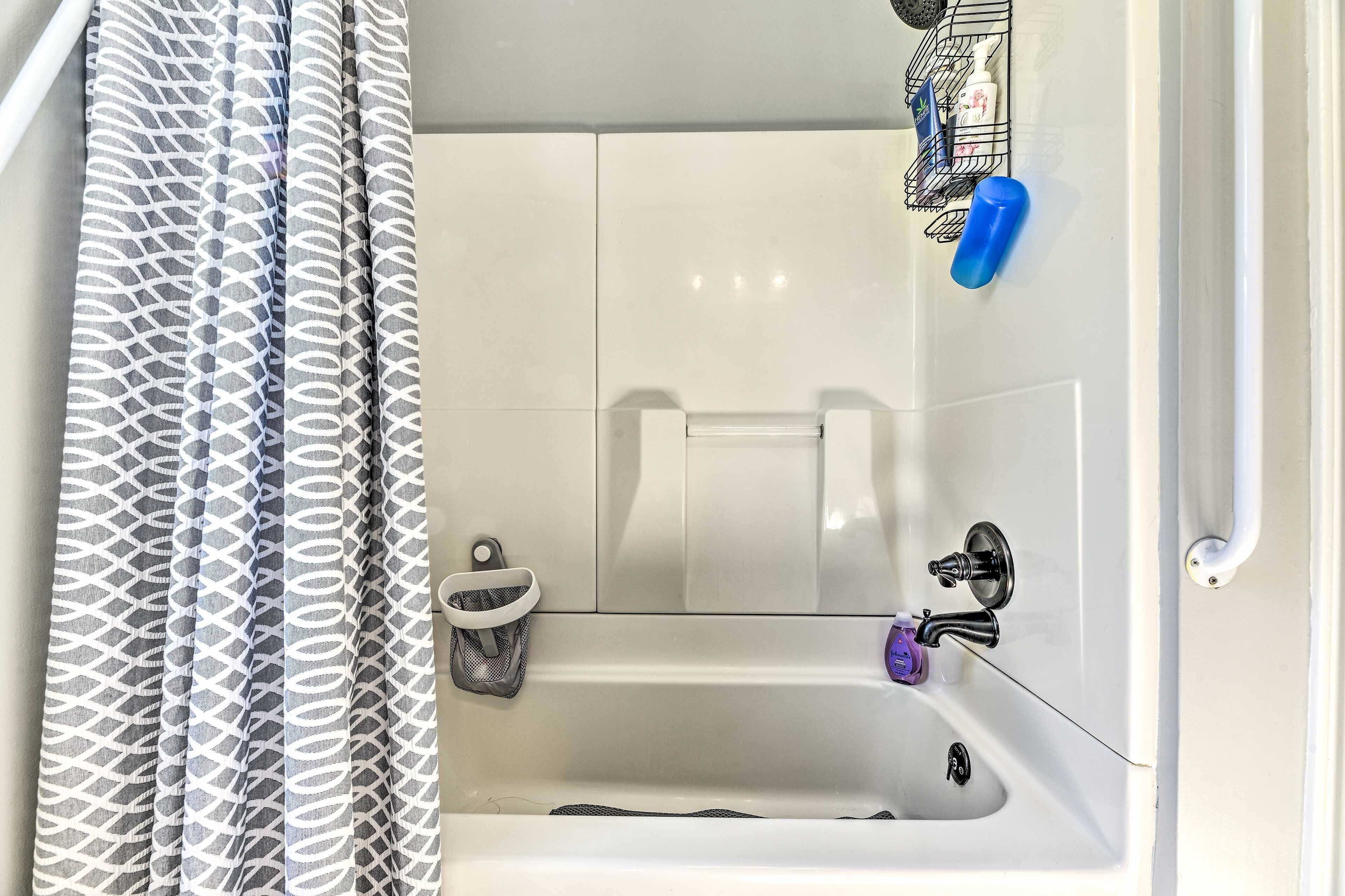 A bathroom with a white bathtub, a shower curtain, a towel rack, and a soap dispenser.