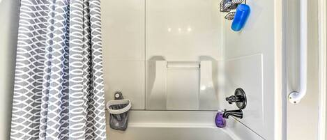 A bathroom with a white bathtub, a shower curtain, a towel rack, and a soap dispenser.