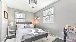 Quarto com cama, mesas de cabeceira, um banquinho, berço e um candelabro.
