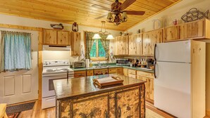 A spacious kitchen with wooden cabinets, a central island, a stove, a refrigerator, and a ceiling fan. - Secluded Farwell Cabin w/ Fire Pit & Gas Grill! (Farwell)