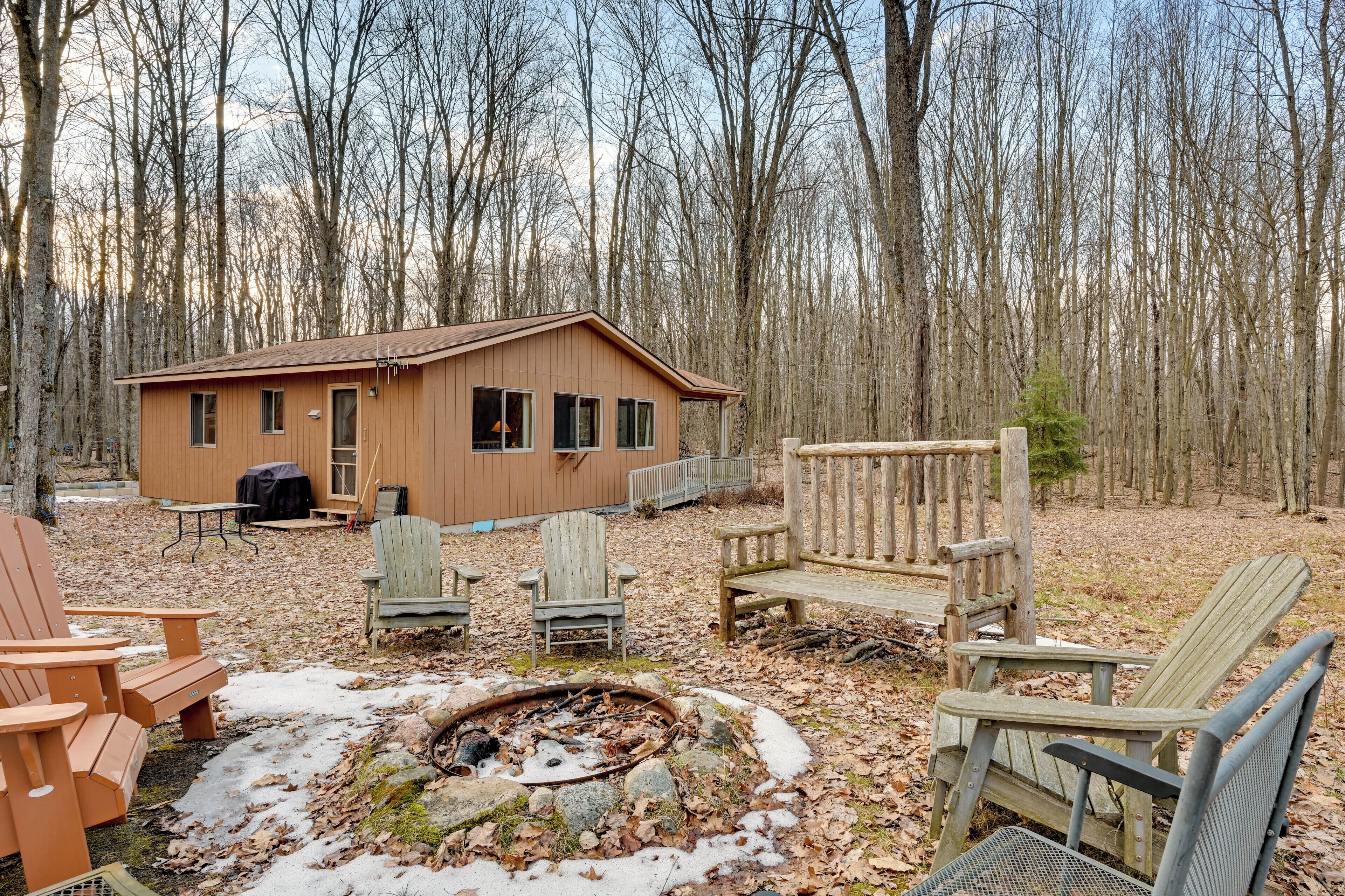 A cabin with a fire pit, several Adirondack chairs, and a table.