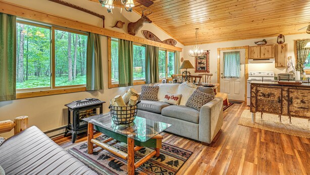 A cozy cabin interior with a wooden ceiling, a fireplace, a sofa, and a kitchen area. - Secluded Farwell Cabin w/ Fire Pit & Gas Grill! (Farwell)