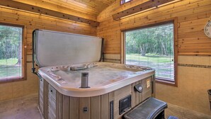 Ein Holzblockhaus-Interieur mit Whirlpool, einem Fenster mit Jalousien und einer Uhr an der Wand.