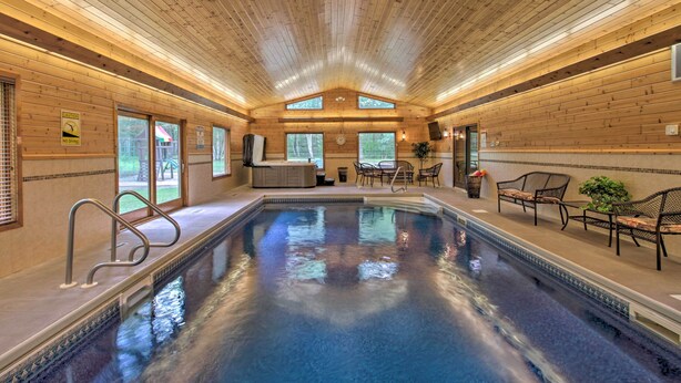 Ein überdachter Pool mit Holzwänden und -decke, eine Sitzecke mit Stühlen und Blick ins Freie durch Fenster.