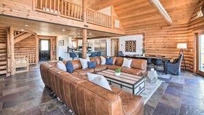 A spacious log cabin interior with a large leather sectional sofa, a dining area, and a balcony.
