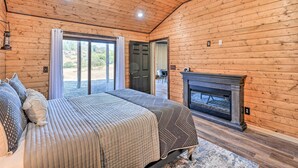 A log cabin bedroom with a bed, a fireplace, and a view through a sliding glass door.