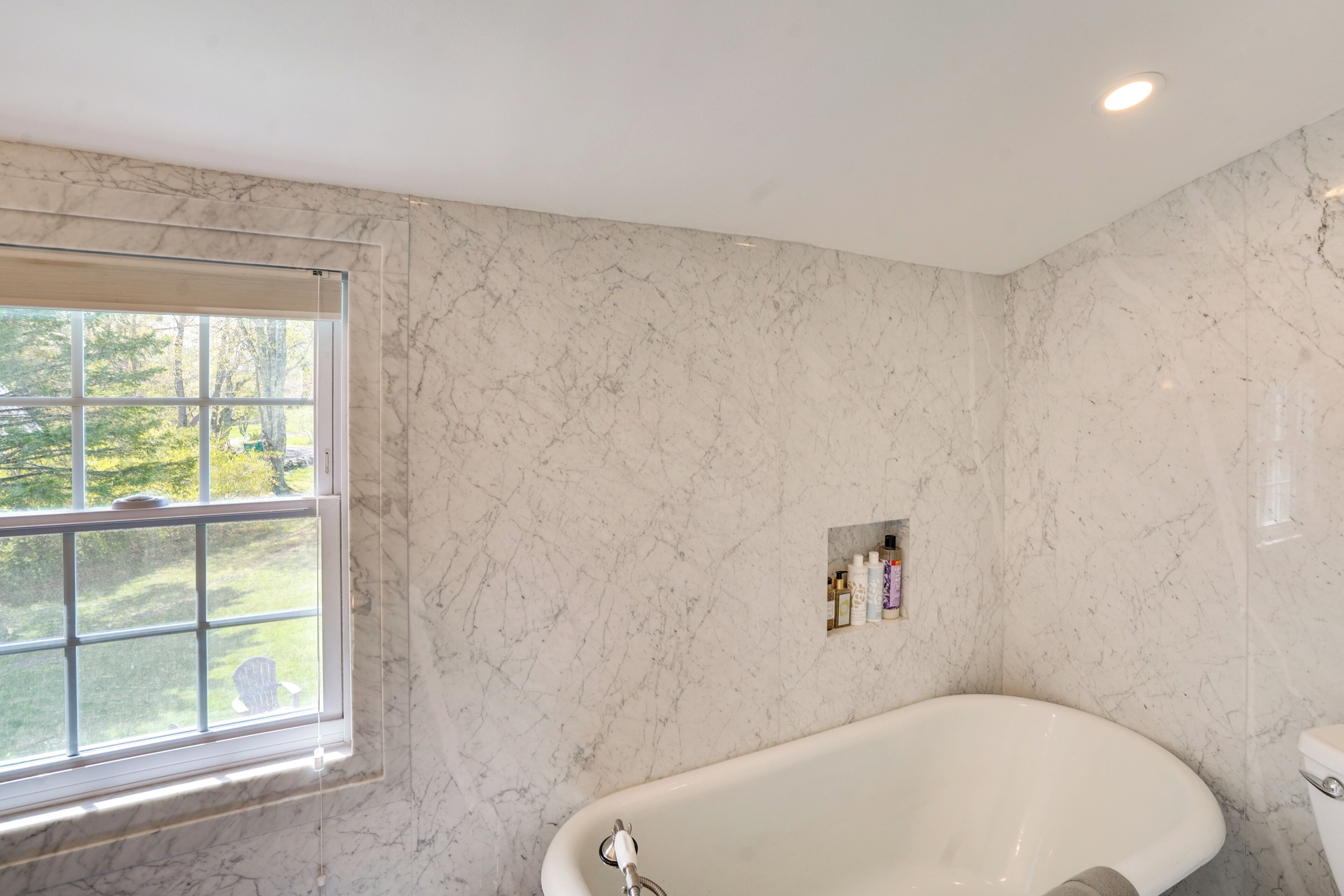 A bathroom with a bathtub, a window, and a marble wall.