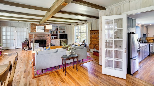 A spacious living area with a fireplace, wooden beams, a sofa, and a kitchen with wooden cabinets. - Quaint Woodstock Escape - 2 Mi to Tinker St! (West Hurley)