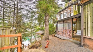 A wooden cabin with a gravel driveway, surrounded by tall trees. - Serene Seldovia Cabin w/ Deck, Grill & Views! (Seldovia)