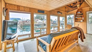 A wooden interior with a large window, a wooden bench, and a television on a stand. - Serene Seldovia Cabin w/ Deck, Grill & Views! (Seldovia)
