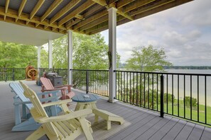 A covered deck with Adirondack chairs, a table, and a grill.