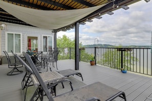 A covered outdoor seating area with tables and chairs, a view of the water, and a railing. - Spacious Baneberry Home w/ Lake Douglas Views! (White Pine)