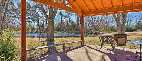 A wooden deck with a table and chairs, overlooking a lake and trees.