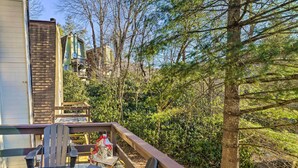 Une terrasse en bois avec une chaise et une table, d’où l’on peut admirer une forêt dense et un immeuble à plusieurs étages doté de balcons.